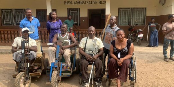 Group of people, some with disabilities, posing outside PoPDA Administrative Block.