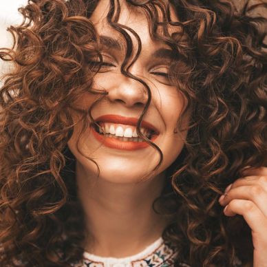 Close-up of a woman joyfully smiling with curly hair covering part of her face.