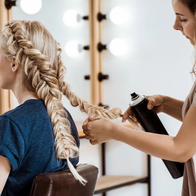 Hairstylist applying hairspray on a blonde braided hairstyle in a salon.
