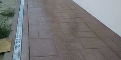 Brown tiled walkway with drainage system alongside a white wall.
