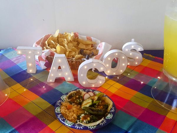 Tacos and chips on a colorful table with illuminated letters spelling TACOS.