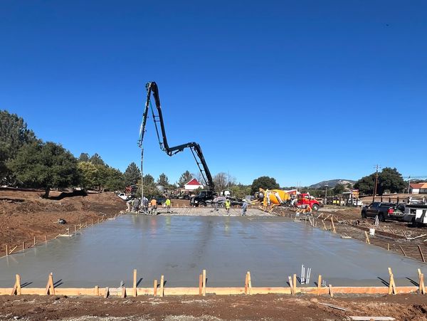 Workers pour concrete on a large flat construction site under clear blue sky.