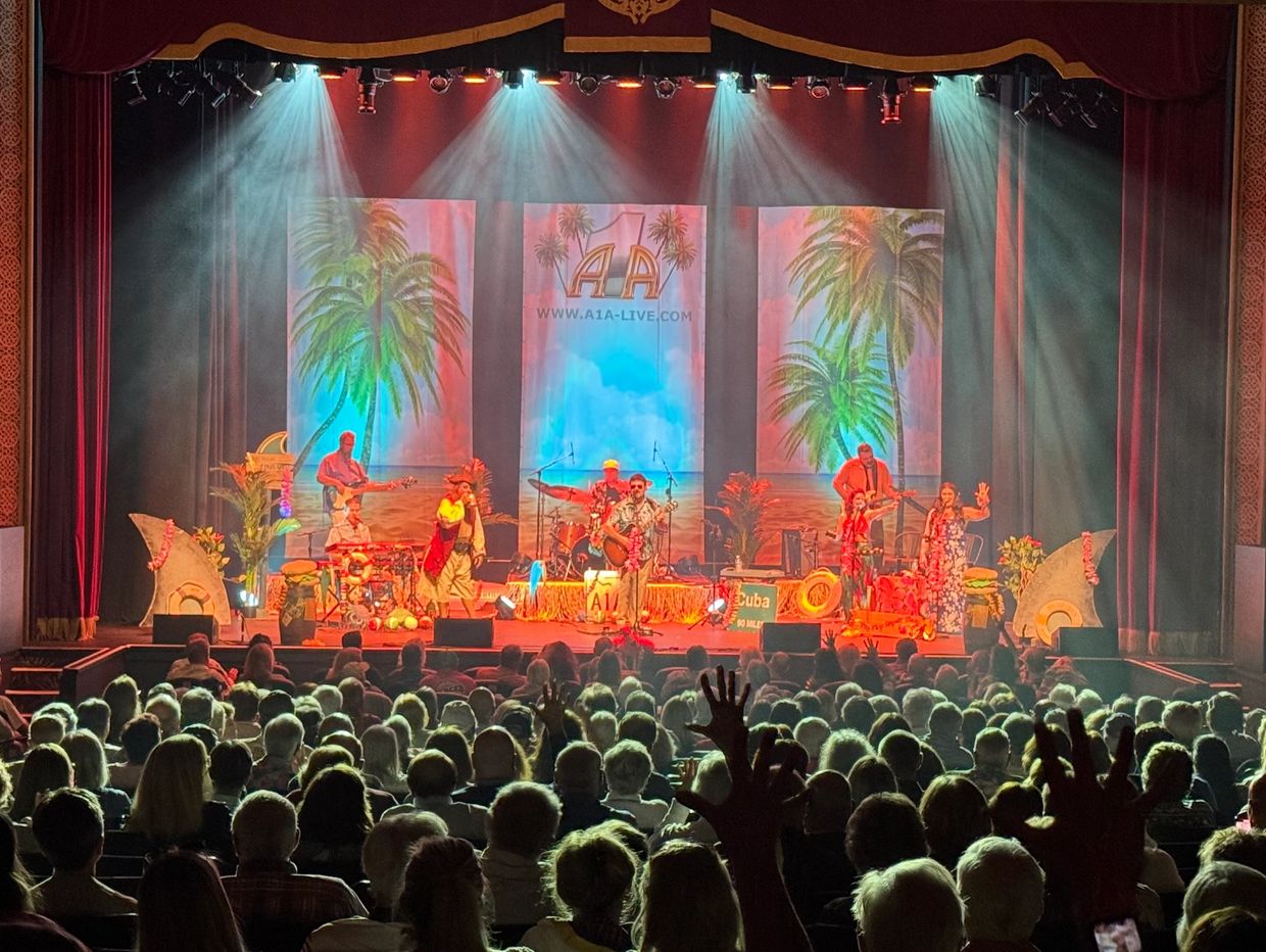 A lively band performs on stage with tropical-themed decorations and a large audience.