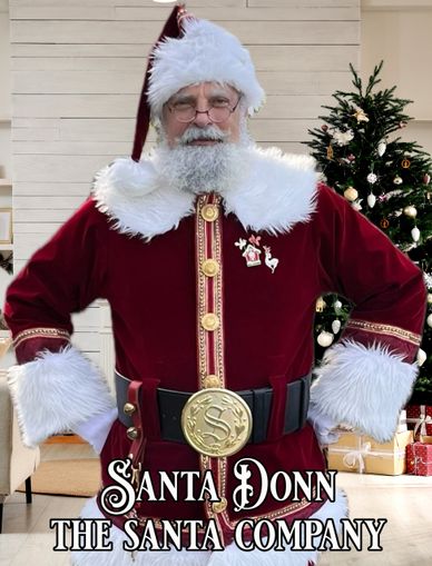 Santa Donn in a festive red suit with white fur trim and a decorated Christmas tree behind him.