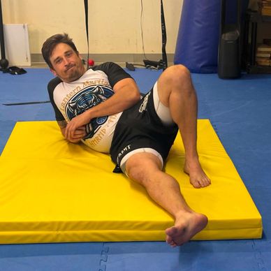 Man relaxing on a yellow mat in a gym.