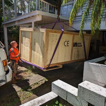 Large wooden crate being lifted into a house under construction.