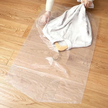 Person placing a garment on a hanger inside a clear plastic garment bag on a wooden floor.