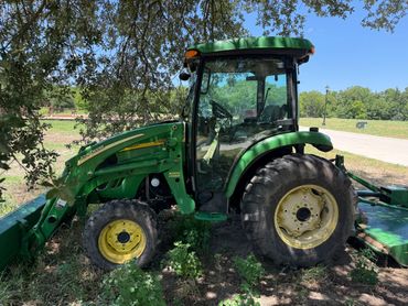 Green John Deere tractor parked under a tree on a sunny day.
