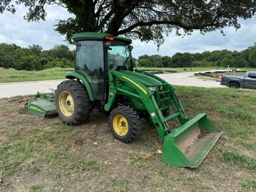 John Deere tractor with front loader parked under a tree.