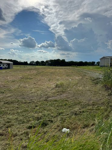 A rural field with mowed grass under a partly cloudy blue sky.