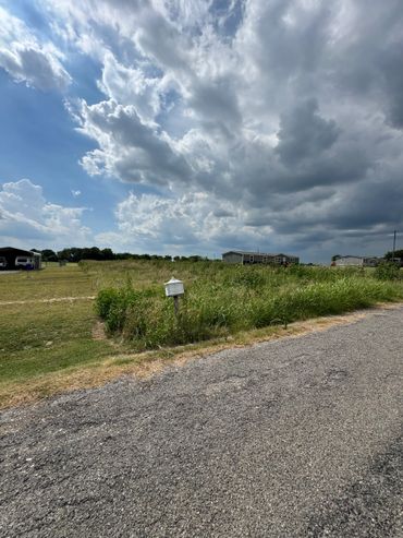 A rural road with overgrown grass and dramatic cloudy sky.