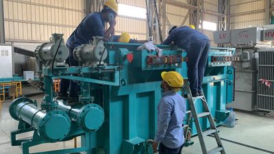 Three workers inspect a large industrial transformer inside a facility.