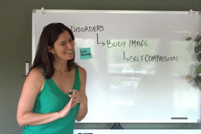 Woman smiling while giving a presentation on body image and self-compassion.