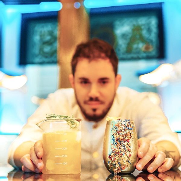 Bartender presenting two creatively garnished cocktails with vibrant decor.