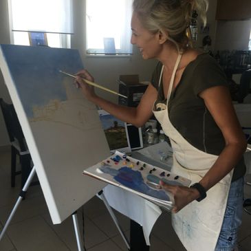 A woman painting on a canvas in a well-lit room.