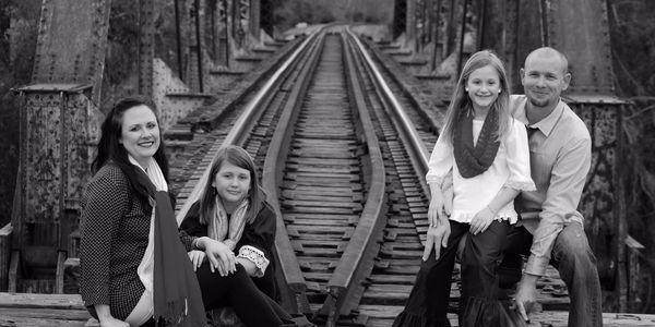 Family of four sitting on railroad tracks, smiling.
