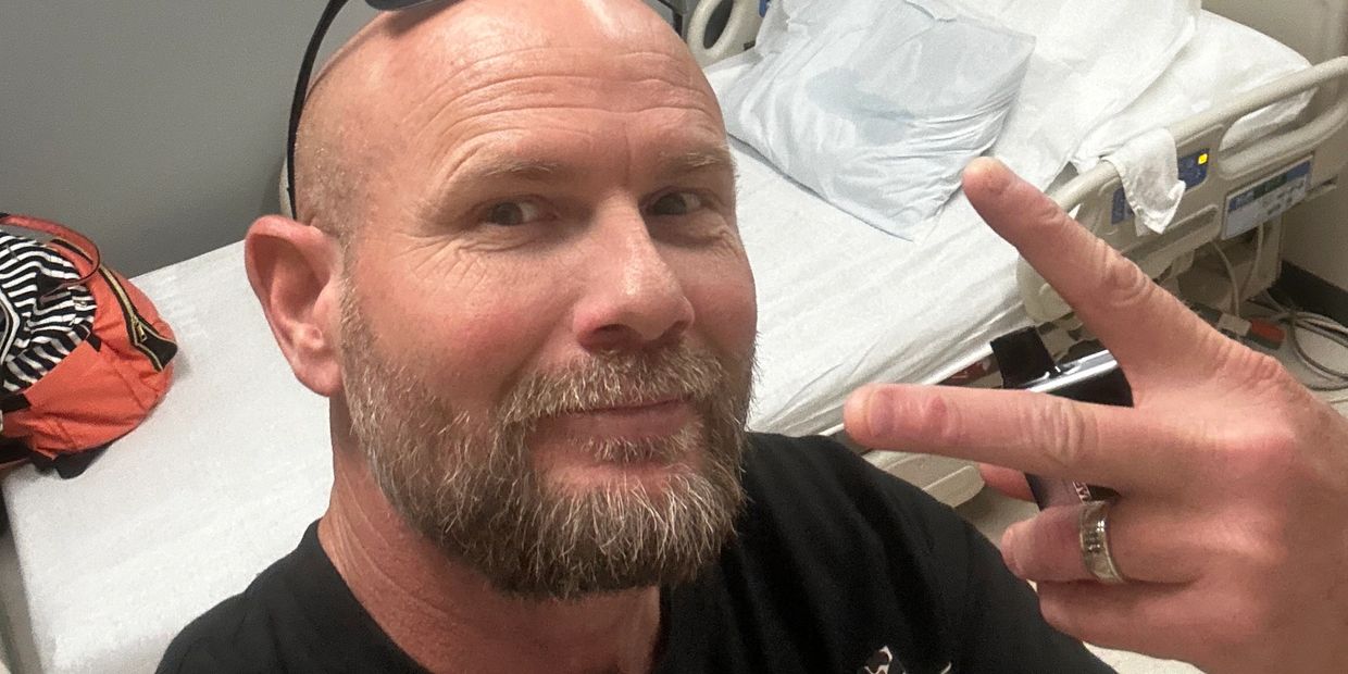 Man with beard making a peace sign in a hospital room.