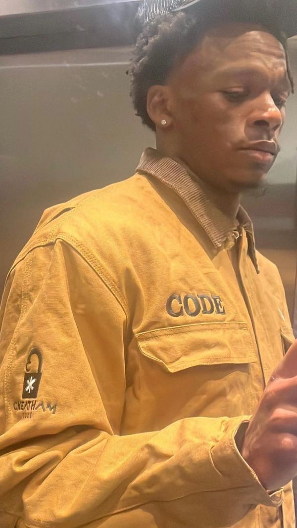 Man wearing a yellow jacket with text embroidered on it.
