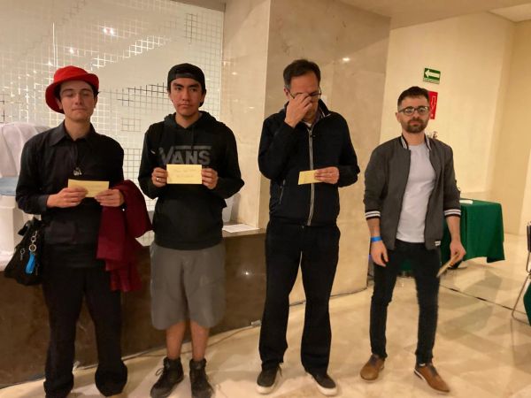 Cuatro hombres sostienen papeles en un lugar interior.