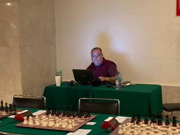 Hombre trabajando en laptop en una sala con mesas de ajedrez.