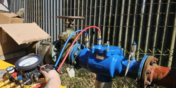 Technician measures pressure on a blue industrial valve with gauges and hoses.