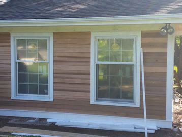 Newly installed windows and cedar siding on an addition with construction materials nearby.