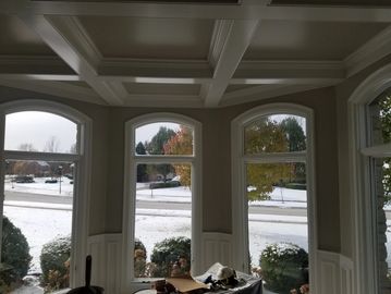 Elegant coffered ceiling above large arched windows overlooking a snowy landscape.