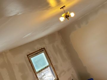 Room under renovation with drywall, paint buckets, and work light.