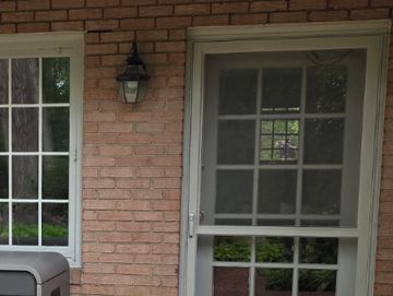 Backyard patio with brick flooring, greenery, and a gray storage box.