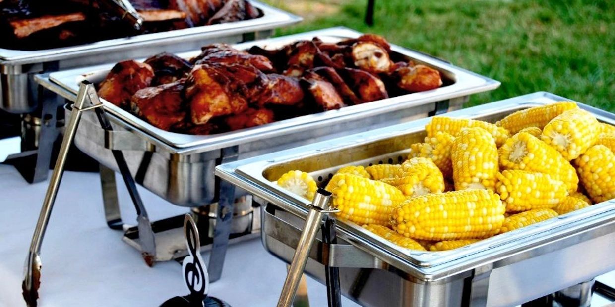 Buffet trays filled with grilled chicken, ribs, and corn on the cob.