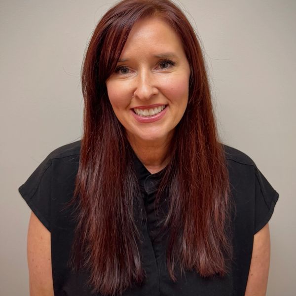 Smiling woman with long reddish-brown hair wearing a black shirt.