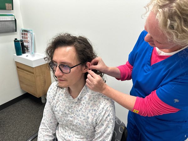 Dr. Cara, audiologist and owner at Rainbow Audiology, fitting hearing aids on a man's ear.