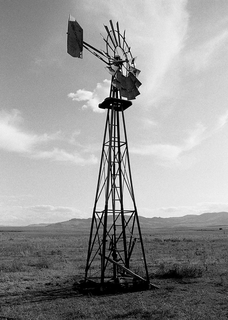 Black and white photo of an old windmill in a vast field under a cloudy sky.