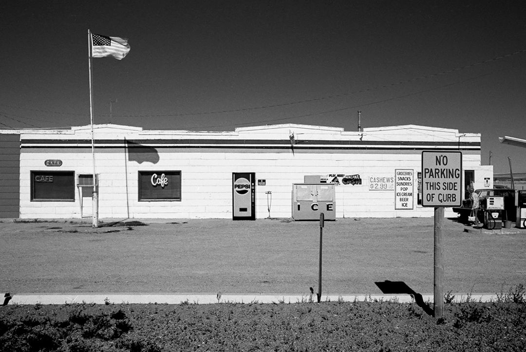 Black and white photo of a cafe with American flag and no parking sign.