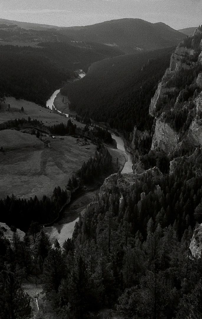 Black and white photo of a winding river through forested mountains.