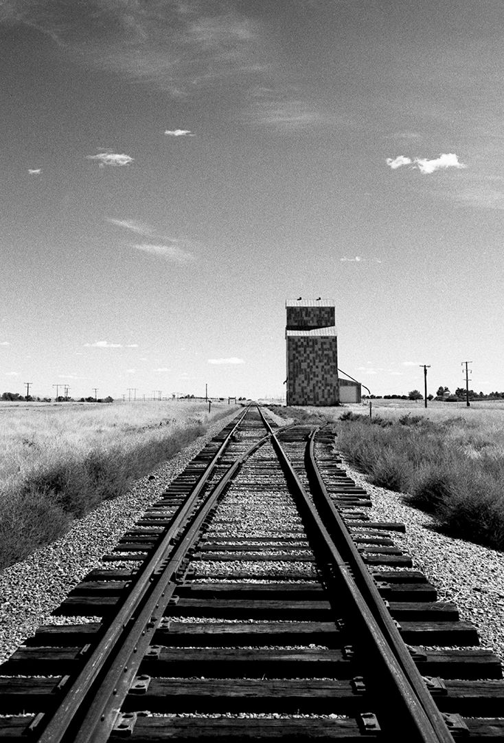 Black and white photo of railway tracks leading to a distant building in an open field.