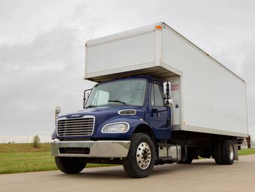 A blue and white delivery truck parked on a concrete road.