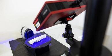 A 3D scanner scanning an object on a turn table. Placed on a white desk with a black work mat. 