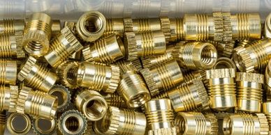 A batch of brass M4 heat inserts inside a small tub. 