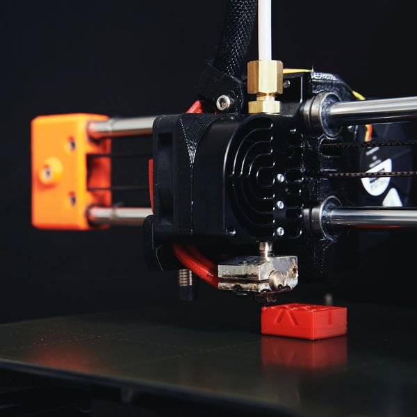 Prusa Mini 3D Printer Hot End Printing a Calibration Cube in Red PLA filament. 
