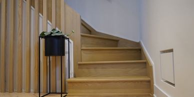 Minimalist wooden staircase with a modern black plant stand beside it.
