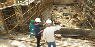 Two construction workers in helmets inspecting a building site with scaffolding.