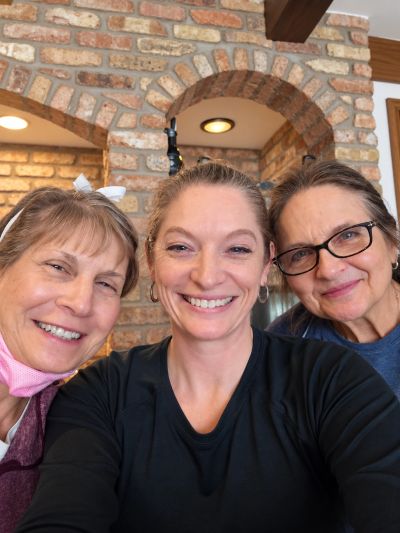 Three smiling women posing for a selfie indoors.