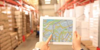 a shipper in a warehouse holding an iPad displaying GPS mapping