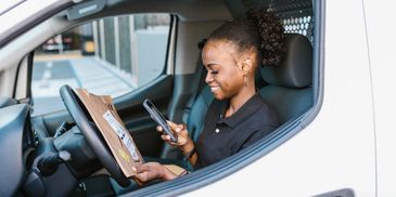 a smiling female courier driver sitting in her van using her phone to scan a package