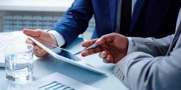 Two businessmen in suits are looking at an iPad, discussing projections