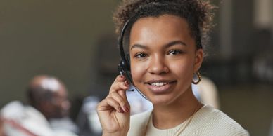 A smiling female customer service representative wearing a headset with her hand on the microphone