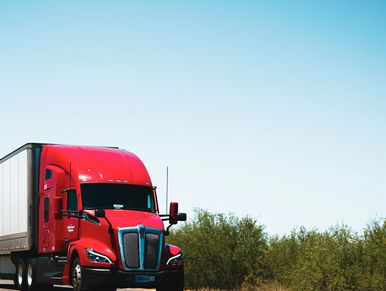 a tractor-trailer driving down the road with brush along the side of the road
