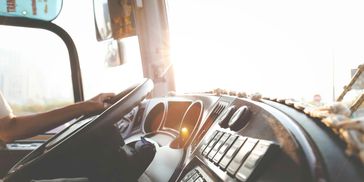 The dashboard of a semi truck at sunset, with a driver behind the wheel looking out of the windshield