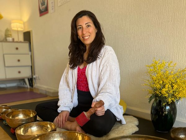 Femme souriante pratiquant la méditation avec bols chantants.